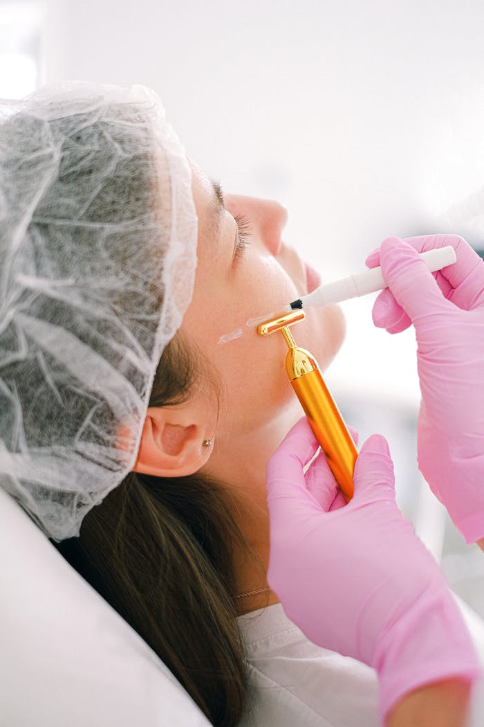 A cosmetologist performs a facial treatment using a golden massage roller and marker.